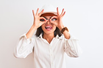 Poster - Young beautiful architect woman wearing helmet and glasses over isolated white background doing ok gesture like binoculars sticking tongue out, eyes looking through fingers. Crazy expression.