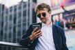 © Svyatoslav Lypynskyy - A Young Guy With Blonde Hair In Sunglasses Looks At His Mobile Phone While Being Outdoors On A Summer Day