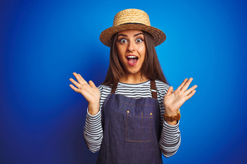 Wall Mural - Young beautiful baker woman wearing apron and hat standing over isolated blue background celebrating crazy and amazed for success with arms raised and open eyes screaming excited. Winner concept