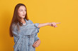 Image of european woamn wearing casual clothes looking far away with opened mouth and points with her fore finger, looks astonished, posing isolated over yellow background. People lifestyle concept.