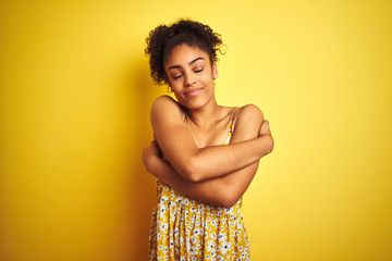 Sticker - African american woman wearing casual floral dress standing over isolated yellow background Hugging oneself happy and positive, smiling confident. Self love and self care