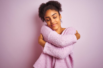 Young african american woman wearing winter sweater standing over isolated pink background Hugging oneself happy and positive, smiling confident. Self love and self care