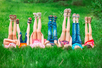 Wall Mural - Children lying on green grass in park on a summer day with their legs lifted up to the sky.