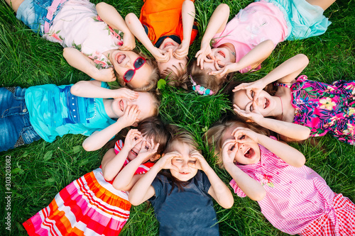 Zdjęcie: A group of children lying on the green grass in the Park. The interaction of the children. A group of children lying on the green grass in the Park. The interaction of the children.