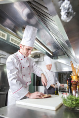 Chef cutting meat on chopping board, professional cook holding knife and cutting meat in restaurant