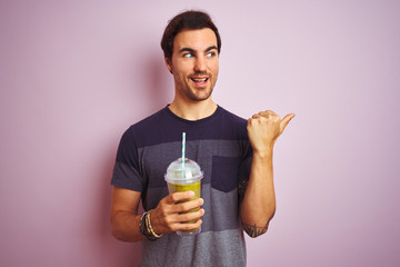 Sticker - Young handsome man with tattoo drinking smoothie standing over isolated pink background pointing and showing with thumb up to the side with happy face smiling