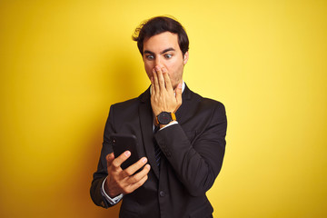 Canvas Print - Young handsome businessman using smartphone standing over isolated yellow background cover mouth with hand shocked with shame for mistake, expression of fear, scared in silence, secret concept