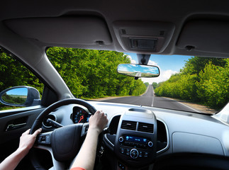 Sticker - Car dashboard with driver's hands on the steering wheel and rear view mirrors on a road in motion with trees against sky with clouds