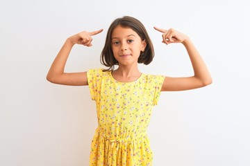 Young beautiful child girl wearing yellow floral dress standing over isolated white background smiling pointing to head with both hands finger, great idea or thought, good memory