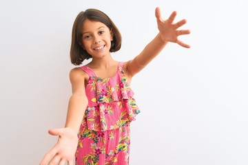 Sticker - Young beautiful child girl wearing pink floral dress standing over isolated white background looking at the camera smiling with open arms for hug. Cheerful expression embracing happiness.