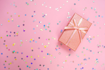 Pink gift box with bibbon and rainbow holographic stars confetti. Minimal flat lay on pink pastel background.