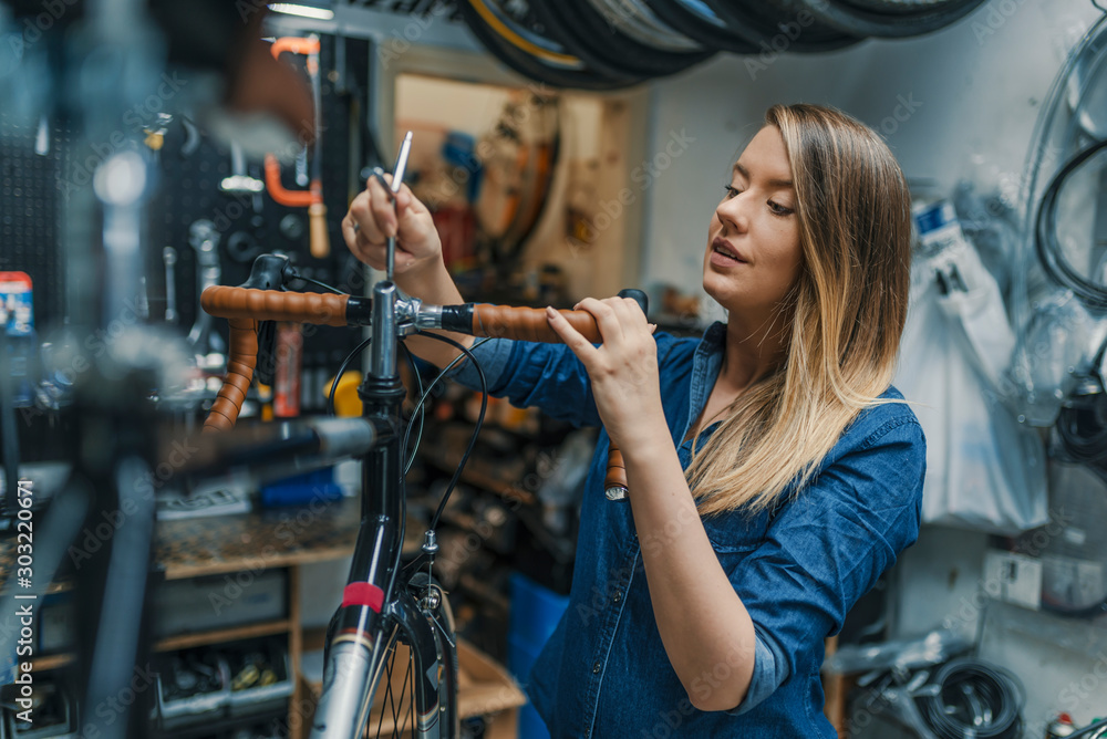 Woman bicycle mechanic is repairing a bike in the workshop - obrazy, fototapety, plakaty 