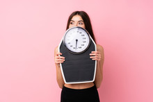Pretty Young Girl With Weighing Machine Over Isolated Pink Background With Weighing Machine And Hiding Behind It