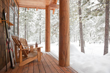 Adirondack Chairs And Skis On Front Porch Of Rustic Upscale Winter Vacation Home Cabin In Snowy Forest