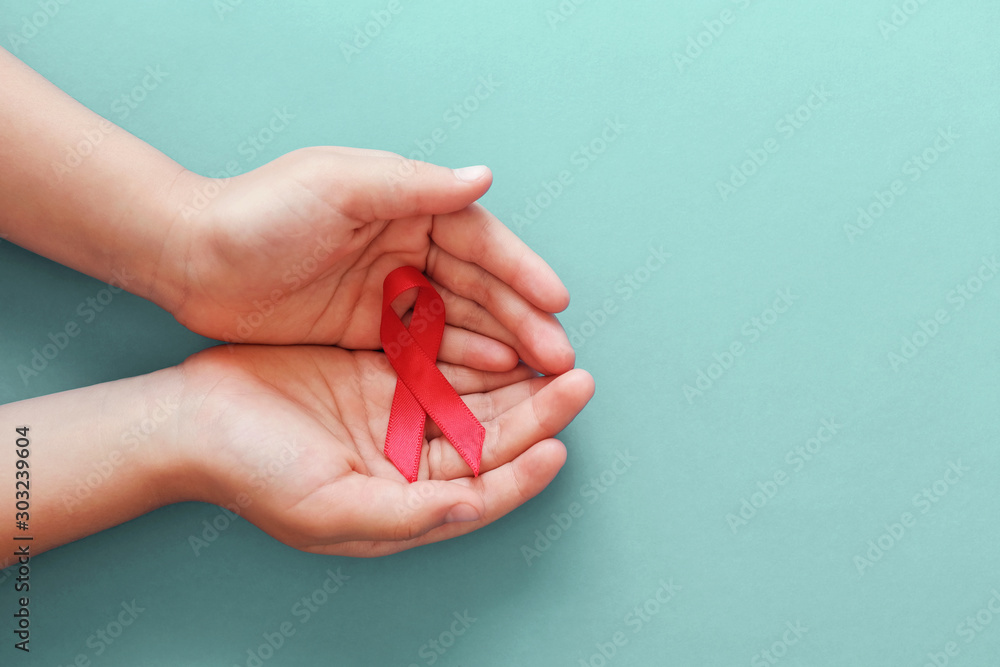 Hands holding red ribbon on blue background, hiv awareness concept, world AIDS day, world hypertension day - obrazy, fototapety, plakaty 