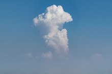 Dramatic White Cumulous Thunder Cloud Rising In A Column Above The Haze Surrounded By Clear Blue Sky And A Few Small Clouds