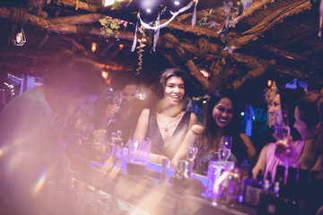 A party of friends in a nightclub at the bar, glamorous young people relax with alcohol.