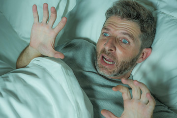  stressed and scared man alone in bed awake at night in fear after having a nightmare feeling paranoid holding the blanket in funny panic face expression