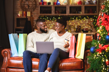 Wall Mural - Cheerful afro couple buying Christmas gifts online