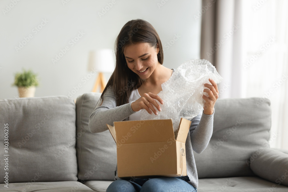 Happy young woman customer open parcel box sit on sofa - obrazy, fototapety, plakaty 