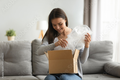 Fotomural Happy young woman customer open parcel box sit on sofa