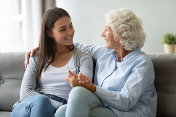 Old grandma and young adult granddaughter talking bonding on sofa