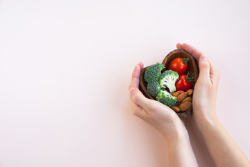 Healthy food for heart on light background. A plate with vegetables and nuts in a woman's hands. Diet and medicine concept. Top view, copy space