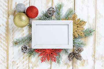 Photo frame between Christmas decoration, with multicolored balls and pine cones on a white wooden table. Top view, frame to copy space