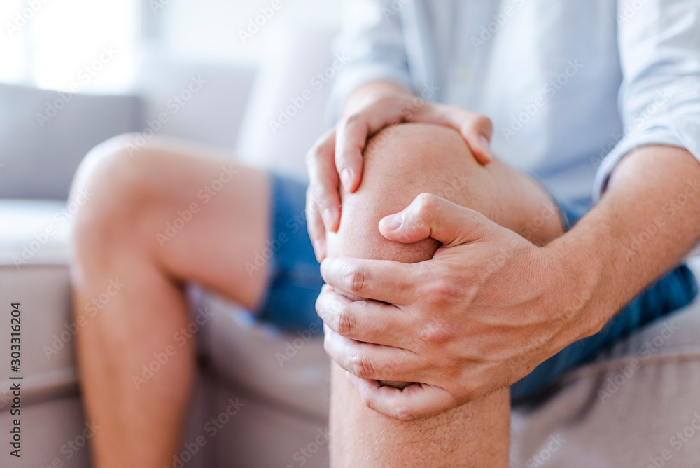 Man suffering from knee pain sitting sofa - obrazy, fototapety, plakaty 