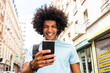 © mimagephotos - smiling young man walking in city and looking at mobile phone