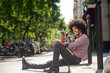 © mimagephotos - Full length side of smiling young guy sitting on floor outside with mobile phone