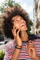 Wall Mural - Close up happy cool young arab guy with afro hair talking with mobile phone and looking up