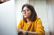 Portrait of pensive business woman wearing glasses at workplace in office. Young handsome female worker using modern laptop