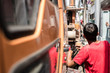 © phoderstock - Back view of truck crane driver wearing red t-shirt is controlling crane working on electric power poles.