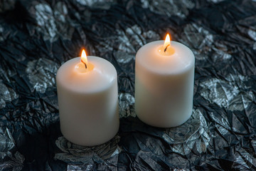 Two lit white candles on dark background.