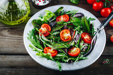 Wall Mural - Mix of fresh green salad leaves with arugula, lettuce, spinach, beets and tomatoes on wooden rustic background.