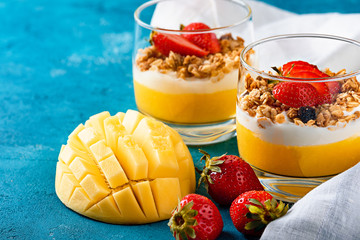 two glass cups with fruit and berry dessert of mango and strawberries with granola and vanilla cream or ricotta