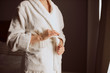 Close shot of gentle tender female hands with beautiful manicure, holding white belt of bathrobe, going to unleash bath clothes, standing by big window, spa beauty concept