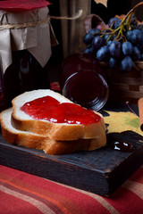 Wall Mural - Grape jelly on a piece of white bread and in glass jars on the wooden board. Autumn still life