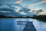 Fototapeta Pomosty - Wooden plank bridge, calm lake and evening clouds on the sky