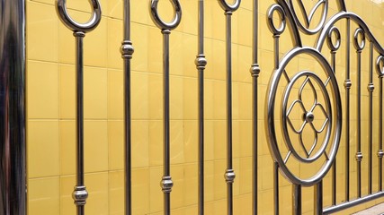 Wall Mural - Side view of the old stainless steel fence with yellow tile wall background in vintage style, exterior architecture decoration design concept