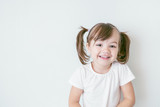 Fototapeta  - portrait of smiling baby girl with ponytails and in a white t-shirt