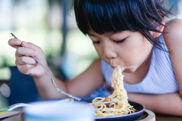 Wall Mural - Hungry face and enjoy eating concept.Little asian girl enjoy eating with spaghetti carbonara with cheese and bacon on a plate in lunch time at restaurant.