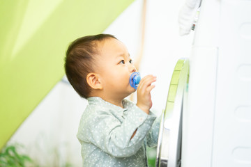 Wall Mural - Family mother and 2 years old asian baby boy suck pacifier little helper in laundry room near washing machine and dirty clothes.