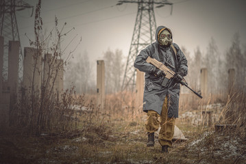 Wall Mural - Soldier with rifle in raincoat and gas mask is walking outdoor.