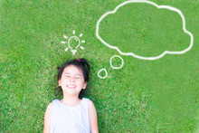 Smart Asian Girl Lay Down On Green Grass And Thinking And Discover Good Creative Idea.World Thinking Day Concept With Girl Kid Having Fun With Dream And Imagination Cloud And Light Bulb Idea.
