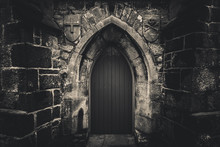 Scary Pointy Wooden Door In An Old And Wet Stone Wall Building With Cross, Skull And Bones At Both Sides In Black And White. Concept Mystery, Death And Danger.