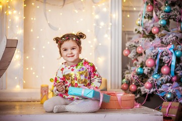 Little girl with two pigtails on the background of a Christmas tree with a gift in her hands.