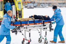Two Paramedics Pushing Sick Unconscious Man On Stretcher Towards Ambulance Car