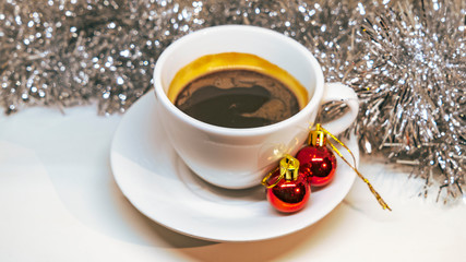 White hot cup of coffee with two christmas tree toys and tinsel. Concept of christmas drink on a white background.